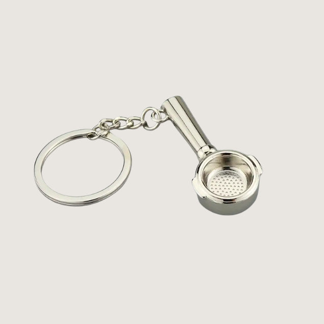 A miniature silver portafilter keychain with a detailed filter basket design, perfect for coffee lovers and baristas.